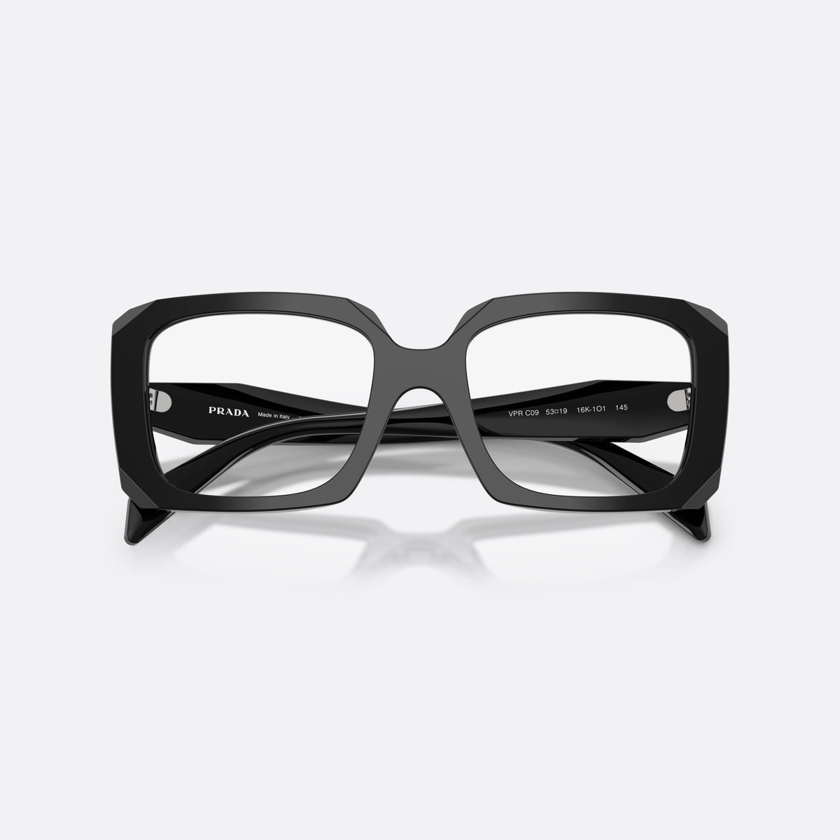 Prada PR C09V 16K1O1 eyeglasses, black pillow frame for women, saddle-like wide bridge, brand lettering on temples, folded